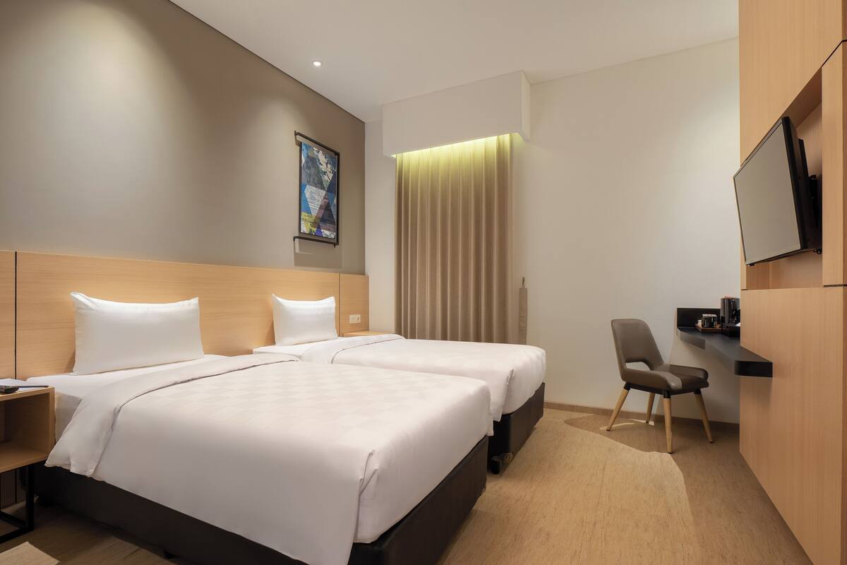 A hotel room with two beds, a desk, a chair, a TV, and a window with curtains.