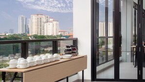 A balcony with a table set with white bowls and a coffee maker, overlooking a cityscape with high-rise buildings. - Hotel 88 Blok M Jakarta by WH (Jakarta)