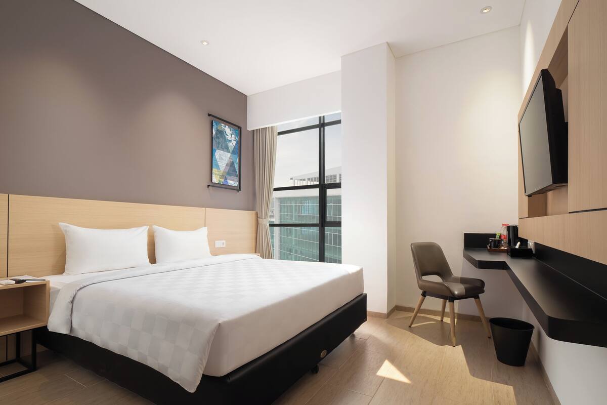A modern hotel room with a large bed, a desk, a chair, and a TV mounted on the wall.