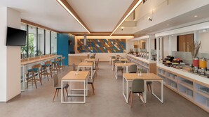 A modern dining area with long tables and chairs, a counter with food displays, and a large wall with geometric patterns. - Hotel 88 Blok M Jakarta by WH (Jakarta)