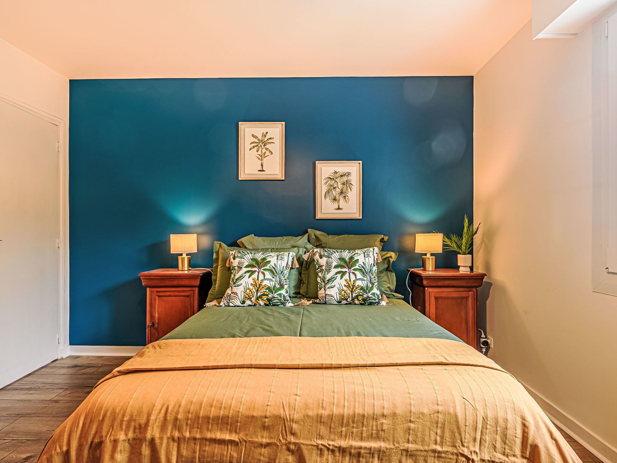 Une chambre à coucher avec un grand lit, une literie verte, deux tables de chevet avec des lampes et deux tableaux encadrés accrochés au mur.