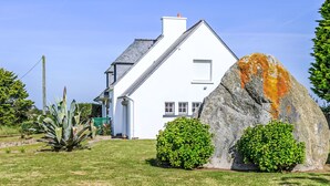 A white house with a sloped roof, a chimney, and a large rock with orange lichen in the front yard. - Villa Colette by Interhome (Plouhinec Morbihan)