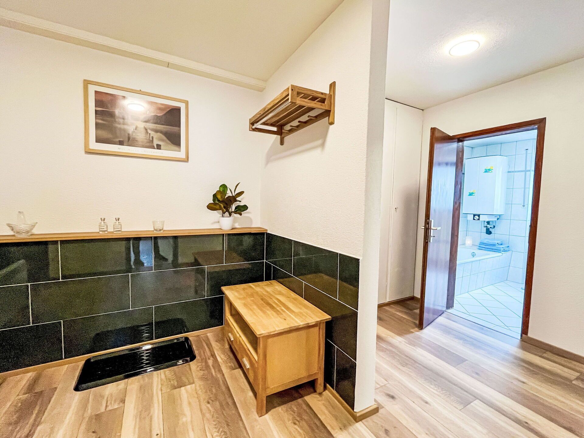 A modern kitchen with black and green tiles, a wooden bench, a sink, and a door leading to a bathroom.