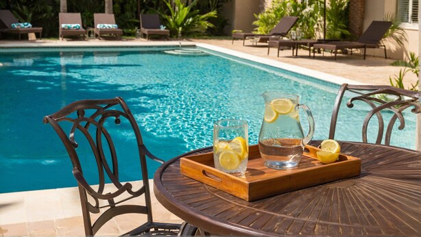Escena junto a la piscina con una mesa, sillas y una jofaina de agua con rodajas de limón.