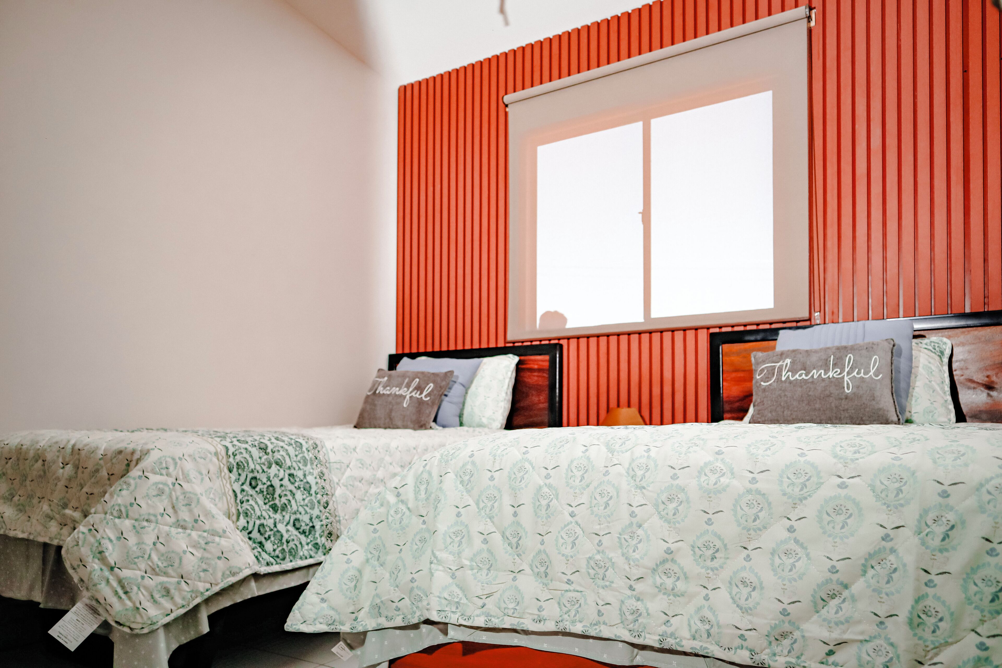 A bedroom with a bed, pillows, a window, and a red wall.