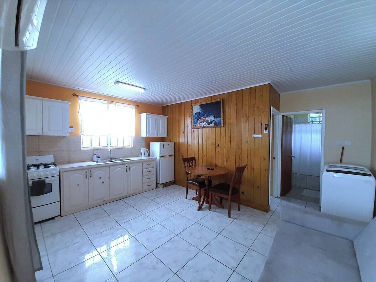 A compact kitchen with white cabinets, a stove, a refrigerator, and a dining area with a table and chairs.
