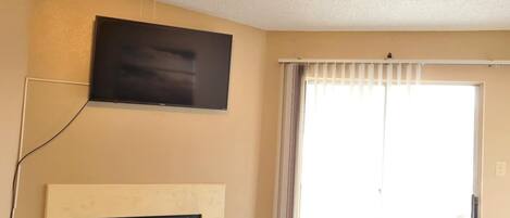 A living room with a fireplace, a ceiling fan, a television mounted on the wall, and a large sliding glass door.