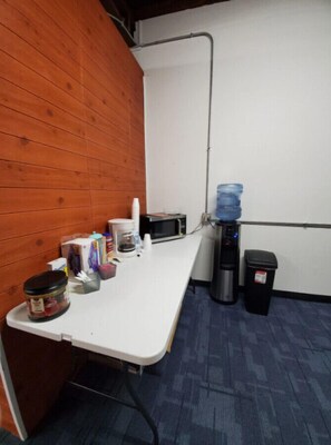 Compact kitchenette with a coffee maker, microwave, and water dispenser.