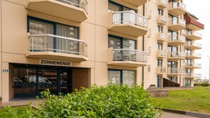 A modern apartment building with balconies, a visible entrance labeled "ZONNEWENDE," and a number "319" on the facade.