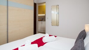Une chambre d’hôtel avec un lit, un tapis à rayures rouges et blanches, un miroir et une vue sur la salle de bain.