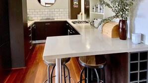 A modern kitchen with a central island, bar stools, a round mirror, and a clock on the wall. - Cosy Manly Beach Hideaway (Manly)