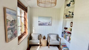 A cozy reading nook with two chairs, a bookshelf, and a large window with artwork. - Cosy Manly Beach Hideaway (Manly)