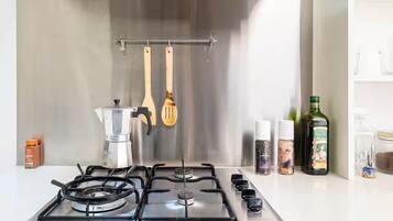A kitchen with a gas stove, hanging utensils, and various kitchen items on the counter.