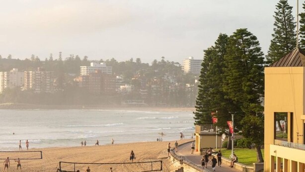 A beach with volleyball players, a volleyball net, and a building with a flag. - Cosy Manly Beach Hideaway (Manly)