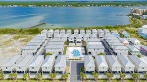 A resort with multiple-story buildings, a central swimming pool, and a view of a large body of water. - 2 min to beach - BBQ | Video Games | Bikes | Pool (Gulf Shores)