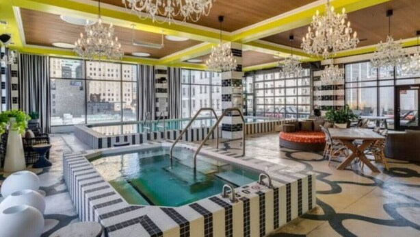 A modern indoor pool area with a hot tub, large chandeliers, and seating areas. - City Club - Unit 429 (Cincinnati)