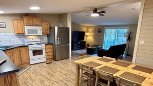 A kitchen with wooden cabinets, a stainless steel refrigerator, and a dining area with a table and chairs. - Whispering River / EV / Mins to Windham and Hunter Mtn (Hensonville)