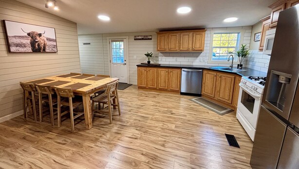 A modern kitchen with wooden cabinets, a stainless steel refrigerator, and a dining area with a wooden table and chairs. - Whispering River / EV / Mins to Windham and Hunter Mtn (Hensonville)