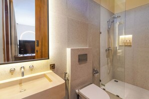 A modern bathroom with a large mirror, a sink, a toilet, and a glass-enclosed shower. - Villa Santa Clara by Pertama Stay (Seminyak)