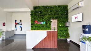A reception desk with a green wall and a wooden counter. - Housr Rushikonda Visakhapatnam (Visakhapatnam)