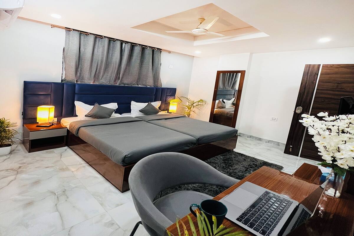 A modern bedroom with a large bed, bedside tables with lamps, a desk with a laptop, and a mirror.