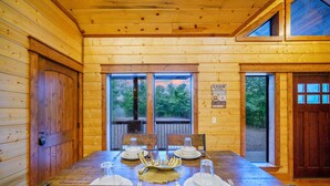 A cabin with a dining table set for four, a wooden interior, and large windows overlooking a deck.