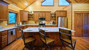 A wooden cabin interior with a kitchen featuring a central island, two chairs, a microwave, a refrigerator, and wooden cabinets.