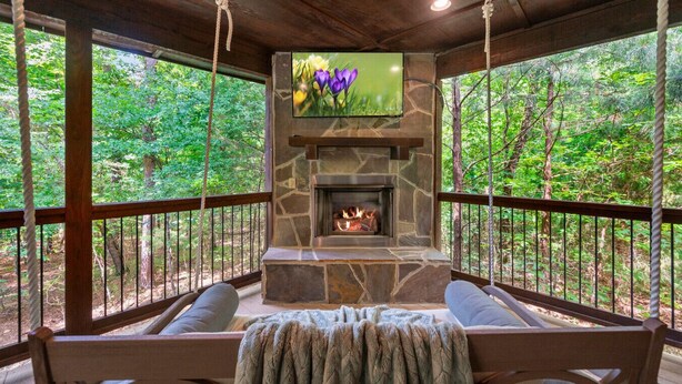 A stone fireplace with a fire, surrounded by wooden seating and a view of a forest.