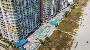 A high-rise hotel with multiple balconies, a pool area with various swimming pools, and a beachside location. -  OCEANFRONT Deluxe 1-BR condo-N. Myrtle Beach. Indoor/outdoor pools-lazy rivers (North Myrtle Beach)