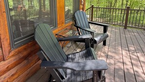 Une terrasse en bois avec deux fauteuils Adirondack et une petite table, donnant sur une zone boisée.