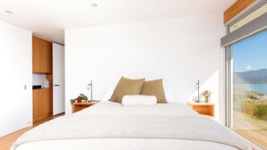 Ein modernes Schlafzimmer mit einem großen Bett, einem Holzschrank, Nachttischen und Blick ins Freie.