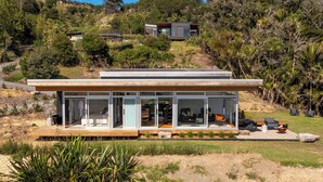 Ein modernes Haus mit großen Glasfenstern, einer Holzterrasse und Sitzgelegenheiten im Freien.