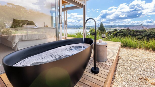 Ein modernes Badezimmer im Freien mit einer großen schwarzen Badewanne, einem Holzterrasse und einem herrlichen Blick auf Berge und einen See.