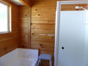 A wooden cabin bathroom with a bathtub, a small stool, and a white door. - Family Cottage on Established Rural Farm. Relaxing, Secluded, has Beautiful View (Broomfield)