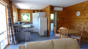 A compact cabin with a kitchenette, a dining area with a table and chairs, and a sofa in the foreground. - Family Cottage on Established Rural Farm. Relaxing, Secluded, has Beautiful View (Broomfield)