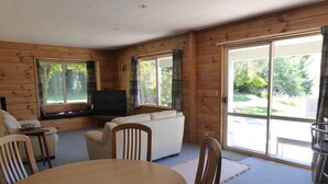 A log cabin interior with a sofa, chairs, a TV, and a dining table. - Family Cottage on Established Rural Farm. Relaxing, Secluded, has Beautiful View (Broomfield)