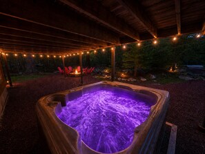 Ein Whirlpool mit violetter Beleuchtung, umgeben von einem überdachten Bereich mit Lichterketten, roten Stühlen und einer Feuerstelle.