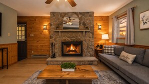 Una sala de estar acogedora con chimenea de piedra, paredes de madera, ventilador de techo y un sofá cómodo.