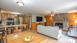 Amplia sala de estar con chimenea de piedra, una mesa de comedor con sillas y una cocina equipada con electrodomésticos modernos.
