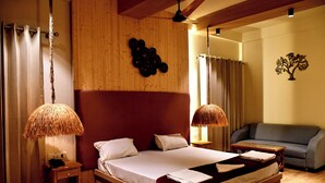 A bedroom with a wooden bed, two bedside lamps, a nightstand, a grey sofa, and a wall art piece. - Hotel Valna Estate Mountain View Kausani By HRG (Kausani)