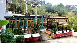 A building with arched windows, a covered outdoor seating area, and potted plants. - Hotel Valna Estate Mountain View Kausani By HRG (Kausani)