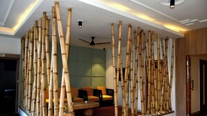 A lobby with bamboo columns, a ceiling fan, and a seating area with orange chairs. - Hotel Valna Estate Mountain View Kausani By HRG (Kausani)