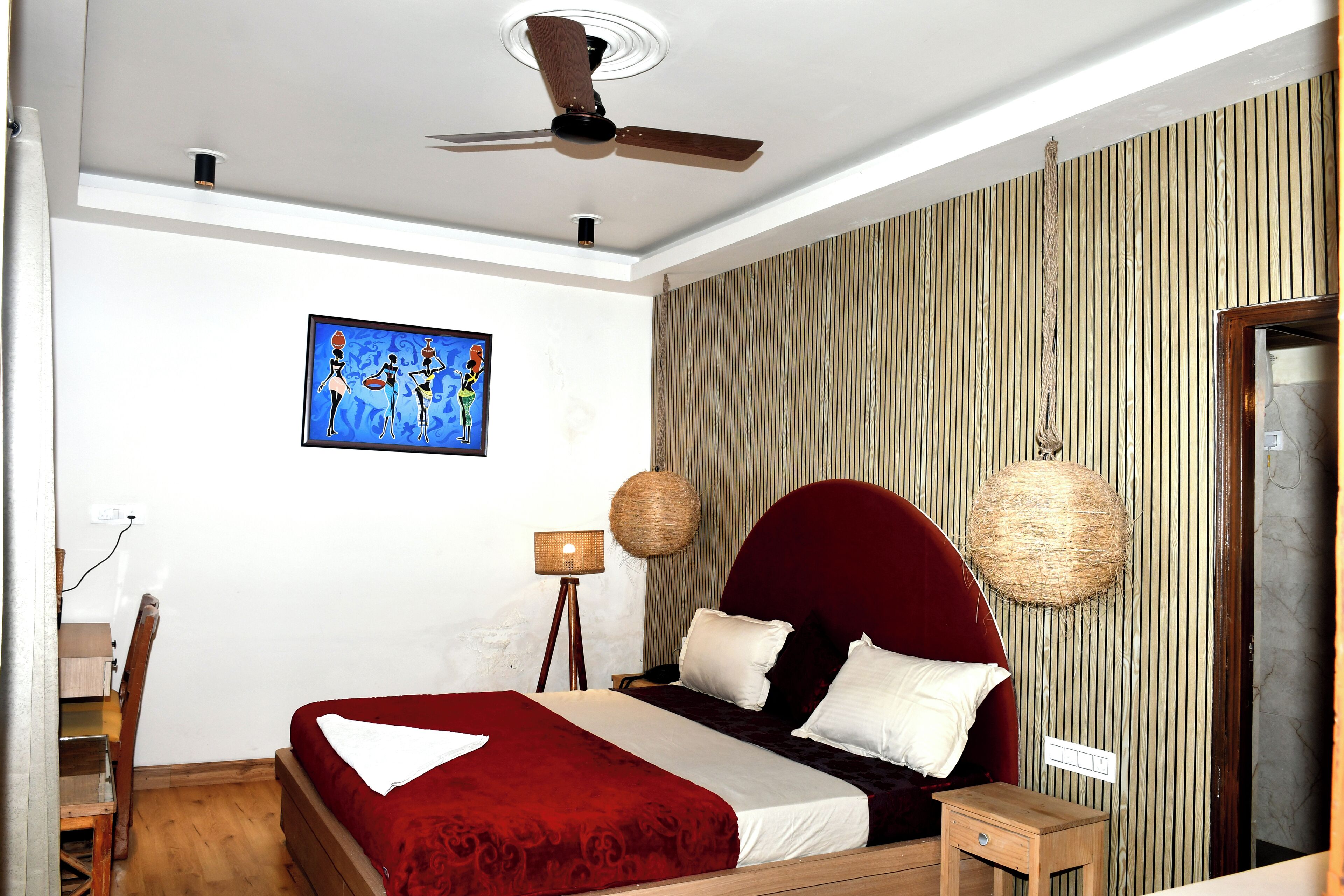 A bedroom with a bed, a ceiling fan, a wall-mounted lamp, and a framed picture.