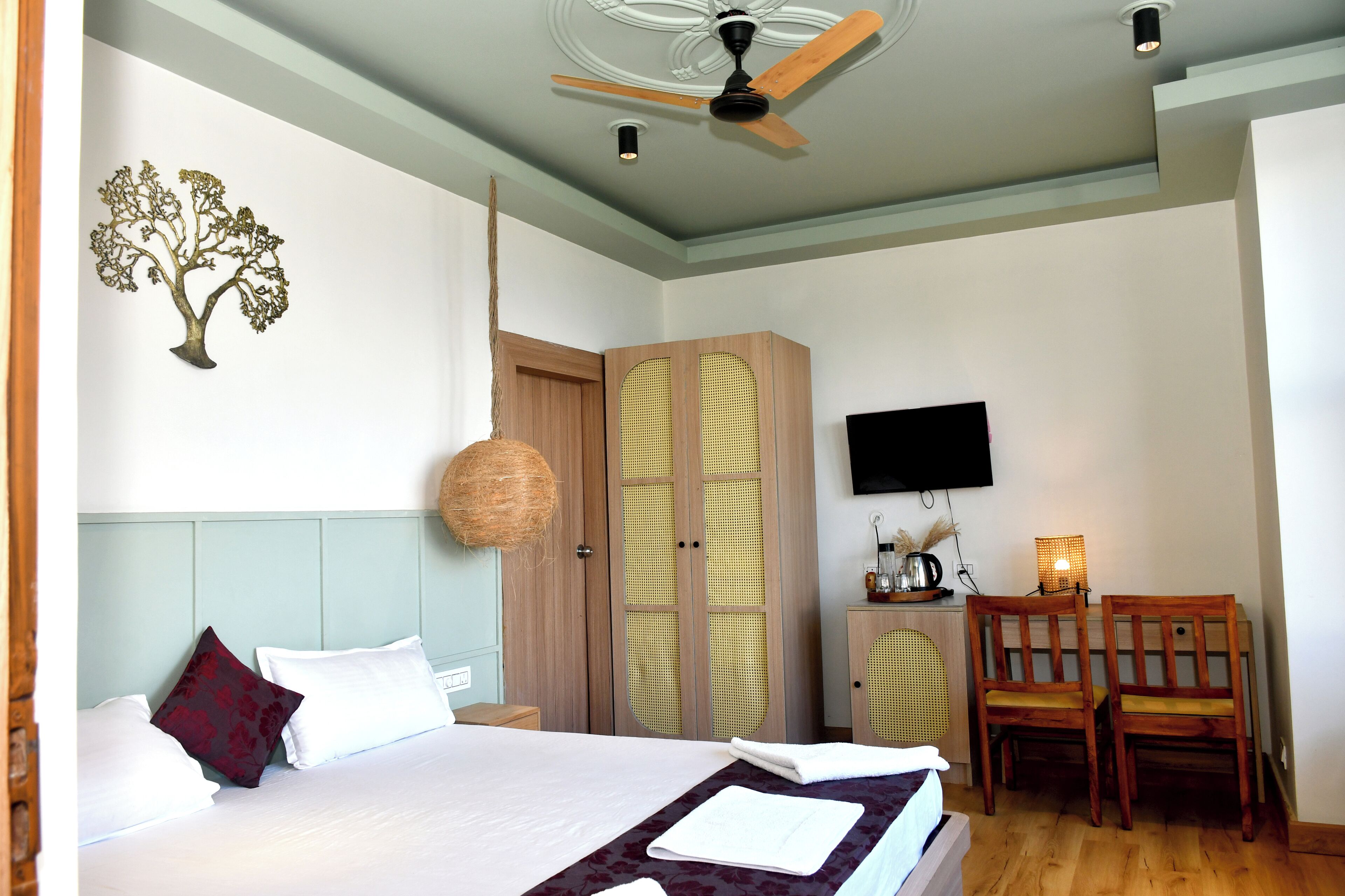 Un dormitorio con cama, ventilador de techo, televisión y escritorio con sillas.