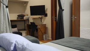 A bedroom with a bed, a desk with a chair, a television mounted on the wall, and a wardrobe.