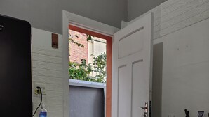A narrow hallway with a door leading to a balcony, a small table with a bottle, and a refrigerator.