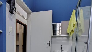 A bathroom with a white sink, a glass shower enclosure, and a yellow towel hanging on the wall.