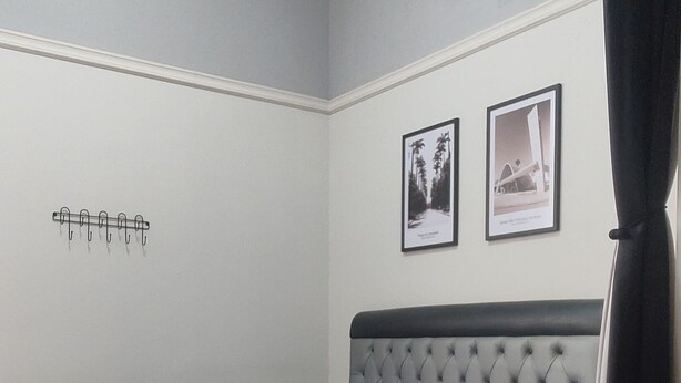A bedroom with a bed, a headboard, a wall-mounted light fixture, and two framed pictures.