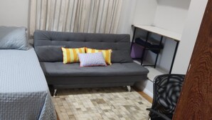 A small, compact room with a grey sofa, a grey bed, and a patterned rug.