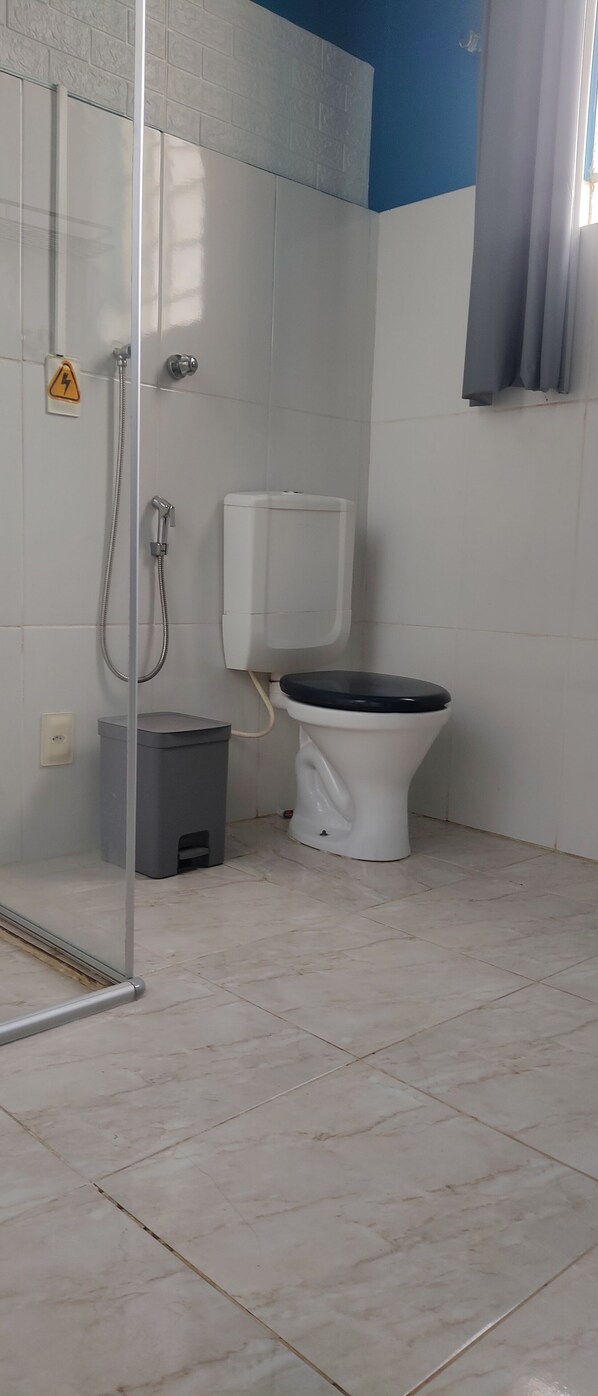 Un baño con ducha, inodoro y cubo de basura.